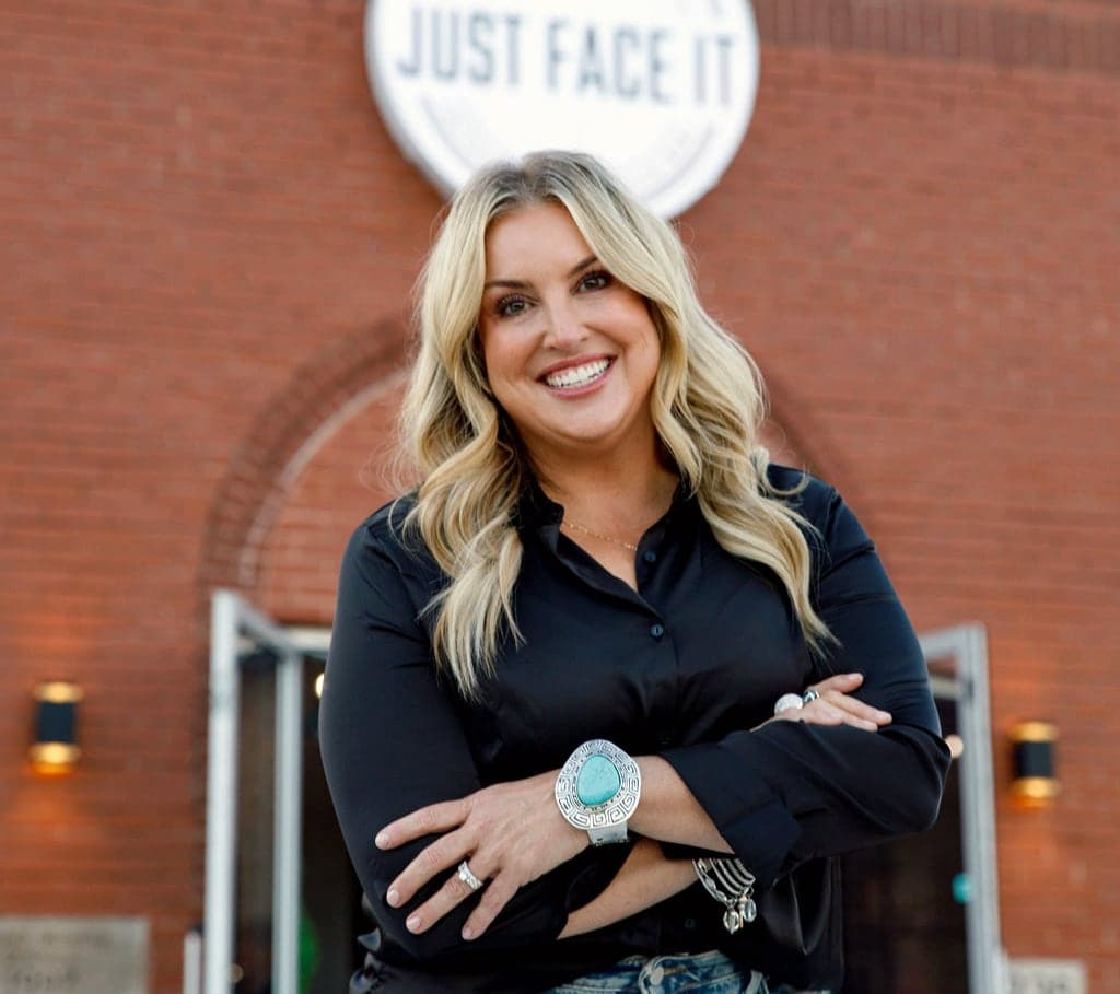 Stephanee Click, RN, MSN, FNP-BC, owner of Just Face It, smiling with her arms crossed outside the salon at dusk
