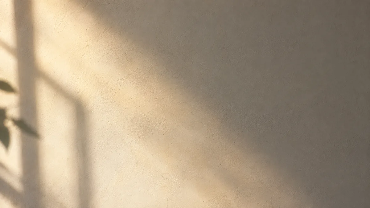 Soft morning light falling across a plain wall in a warm diagonal band, with the edge of the light fading gradually, representing uneven skin tone