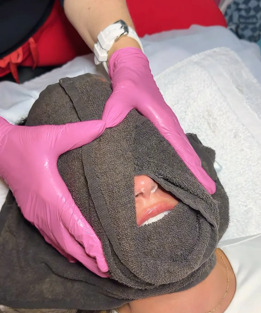 Gloved hands pressing a warm towel over a client's face during a facial