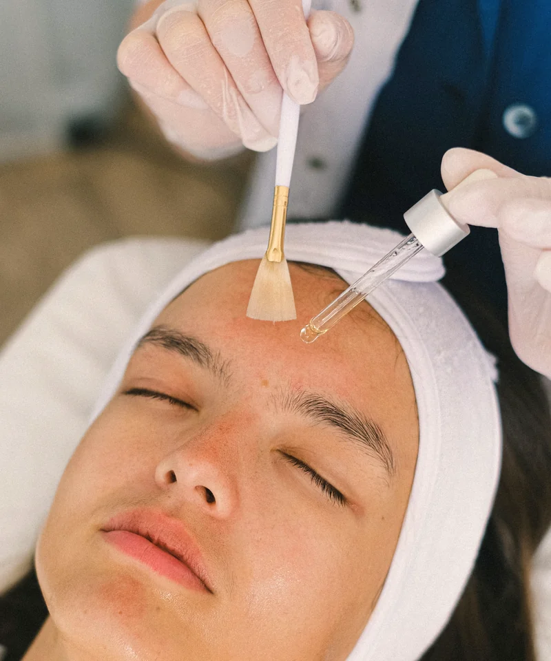 An esthetician brushing a peel solution onto a client's forehead